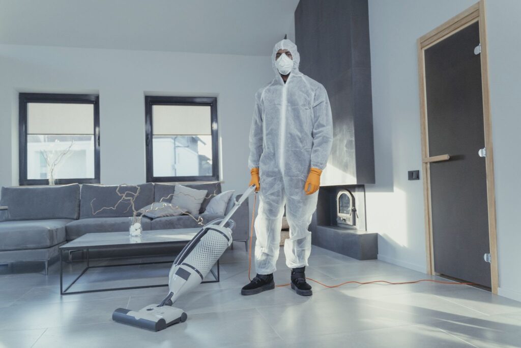 A cleaner in personal protective equipment cleans the floor of a living room.